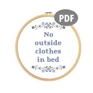 Peut inclure: Un cerceau de broderie blanc avec un motif de point de croix qui dit "No outside clothes in bed" avec une bordure de fleurs violettes et jaunes.