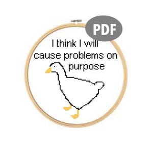 May include: A white goose with a yellow beak and feet, in a wooden embroidery hoop. The text "I think I will cause problems on purpose" is written above the goose.