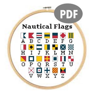May include: A cross-stitch pattern of nautical flags, displayed in a wooden embroidery hoop. The flags are in various colors and patterns, each representing a letter of the alphabet. The text "Nautical Flags" is above the flags, and a "PDF" graphic is in the upper right.
