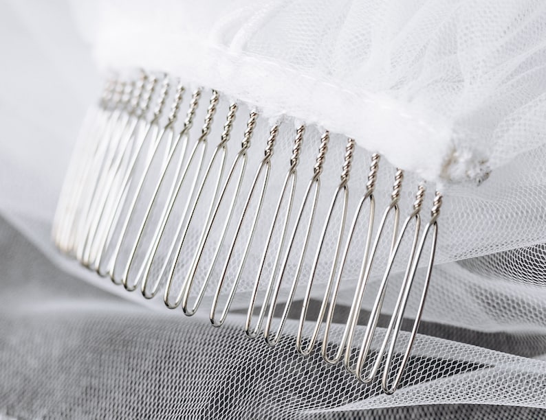 May include: A close-up of a silver comb with a row of teeth. The comb is attached to a white tulle fabric.