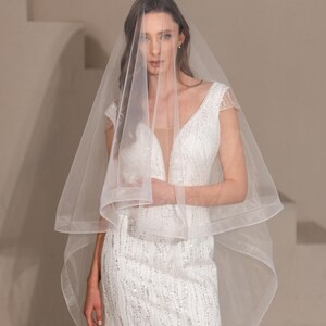 May include: A bride wearing a white wedding dress with a sequined bodice and a long veil. The veil is sheer and has a scalloped edge.