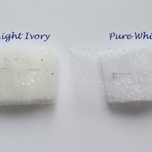May include: Two swatches of tulle fabric with glitter, one in light ivory and one in pure white. Both swatches are pinned with a straight pin.