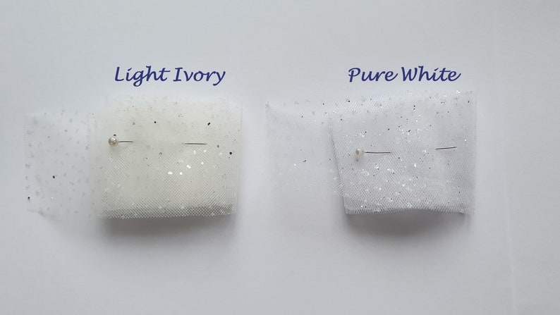 May include: Two swatches of tulle fabric with glitter, one in light ivory and one in pure white. Both swatches are pinned with a straight pin.