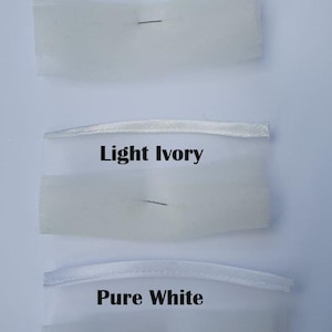 May include: Three fabric swatches labeled Ivory, Light Ivory, and Pure White. Each swatch consists of a thin satin ribbon strip attached to a piece of sheer, fine-mesh tulle fabric. The colors transition from a warm off-white to a bright white.