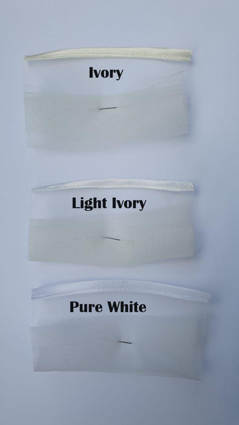 May include: Three fabric swatches labeled Ivory, Light Ivory, and Pure White. Each swatch consists of a thin satin ribbon strip attached to a piece of sheer, fine-mesh tulle fabric. The colors transition from a warm off-white to a bright white.