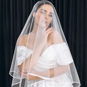 May include: A bride wearing a white wedding dress and a white veil. The veil is covering her face and she is looking down.