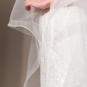 May include: A white wedding dress with a sheer veil. The dress is covered in sequins and has a fitted bodice.