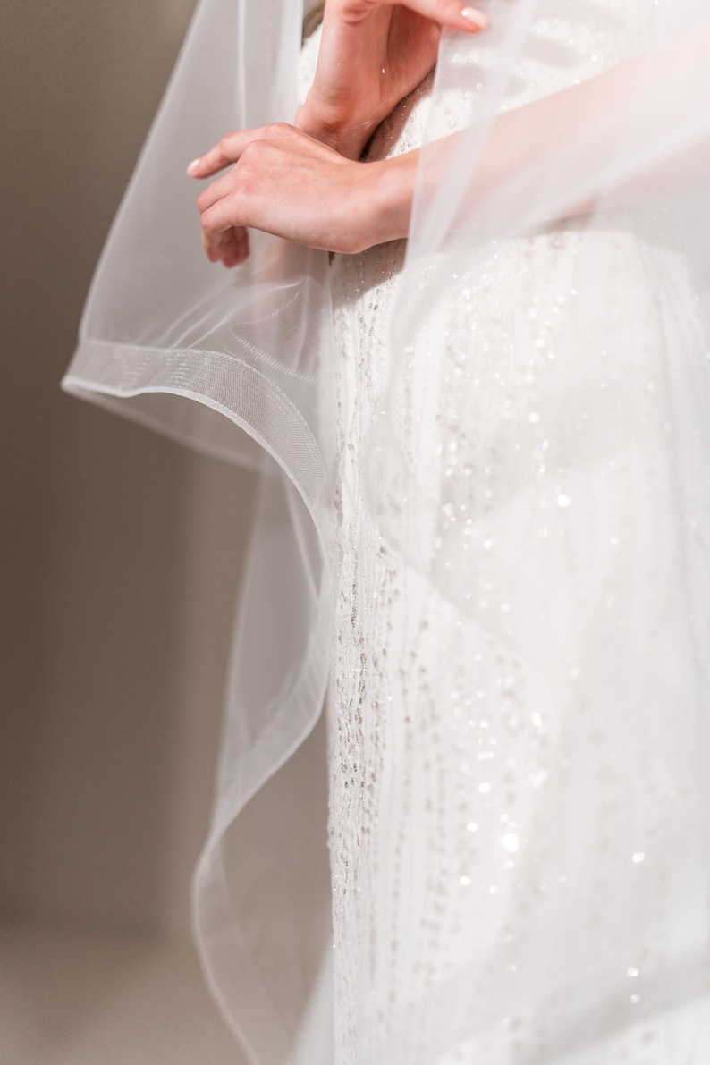 May include: A white wedding dress with a sheer veil. The dress is covered in sequins and has a fitted bodice.