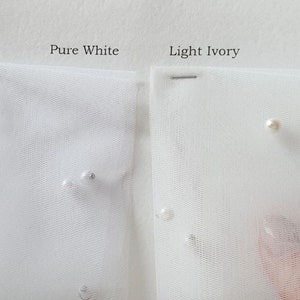 May include: Two swatches of tulle fabric, one labeled "Pure White" and the other "Light Ivory". Both swatches have small pearl-like embellishments.