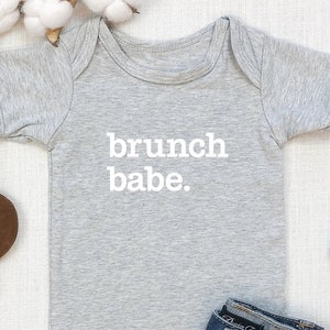 Può includere: Body da neonato grigio con testo bianco che dice "brunch babe."