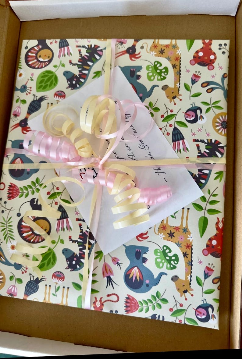 May include: A square gift package wrapped in cream-colored paper featuring a colorful pattern of stylized animals, flowers, and leaves. The package is tied with pale pink and yellow curling ribbons and includes a white card with handwritten text.