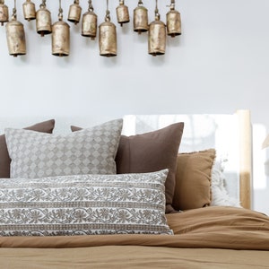 May include: A bed with a brown duvet cover and several pillows. The pillows are a mix of brown, white, and gray. There are decorative bells hanging from the ceiling above the bed.