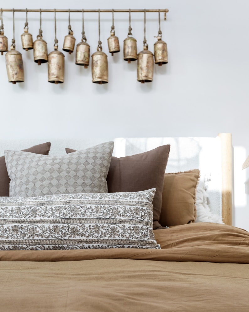 May include: A bed with a brown duvet cover and several pillows. The pillows are a mix of brown, white, and gray. There are decorative bells hanging from the ceiling above the bed.