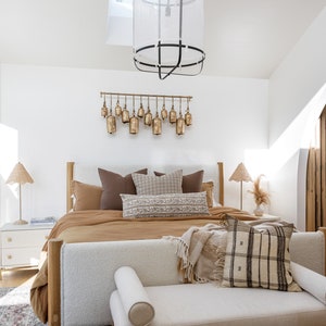 May include: A bedroom with a large bed with a brown duvet and white and brown pillows. There is a white bench at the foot of the bed with a brown and white throw blanket and a brown and white pillow. There is a large window with a view of trees and a skylight in the ceiling.