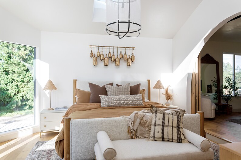 May include: A bedroom with a large bed with a brown duvet and white and brown pillows. There is a white bench at the foot of the bed with a brown and white throw blanket and a brown and white pillow. There is a large window with a view of trees and a skylight in the ceiling.