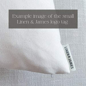 May include: White linen pillow with a small black and white woven label that reads "LINEN & JAMES"