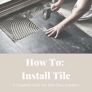 May include: A person installing dark gray floor tiles using a rubber mallet. The tile is being placed on a bed of gray mortar. The text "How To: Install Tile" is displayed on a beige background below the image. The text "A Complete Guide For First Time Installers" is displayed below the title.
