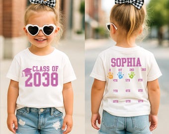 Könnte beinhalten: Ein Kind trägt ein weißes T-Shirt mit dem lila Schriftzug "CLASS OF 2038". Das Kind trägt auch Jeansshorts, herzförmige Sonnenbrillen und eine schwarz-weiße Schleife. Auf der Rückseite des T-Shirts stehen der Name "SOPHIA" und Handabdrücke.