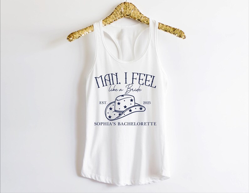 Puede incluir: Camiseta blanca de tirantes con un gr&aacute;fico azul que dice "Man, I feel like a Bride" con un sombrero de vaquero y estrellas. El texto tambi&eacute;n dice "Est. 2025" y "Sophia's Bachelorette."