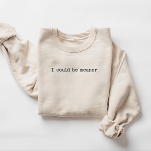 May include: A beige sweatshirt with the text "I could be meaner" in black, centered on the front. The sleeves are rolled up. The sweatshirt is made of a soft material and is displayed on a white background.