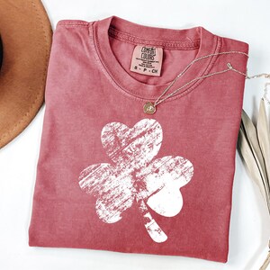 May include: A red t-shirt with a white distressed shamrock graphic. The shirt is made of a soft, comfortable fabric.