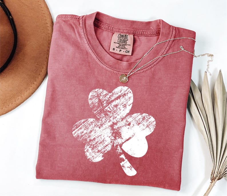 May include: A red t-shirt with a white distressed shamrock graphic. The shirt is made of a soft, comfortable fabric.