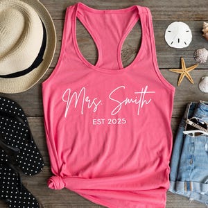 Pu&ograve; includere: Canotta rosa con il testo "Mrs. Smith EST 2025" in bianco.