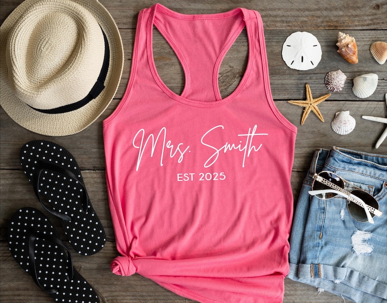 Pu&ograve; includere: Canotta rosa con il testo "Mrs. Smith EST 2025" in bianco.