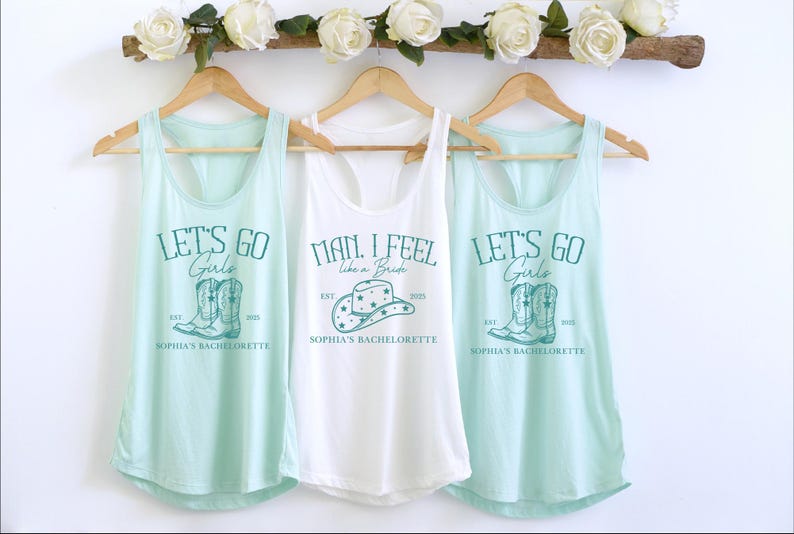 Puede incluir: Tres camisetas sin mangas con un tema de despedida de soltera. La camiseta blanca dice "Man, I feel like a bride" con un gr&aacute;fico de sombrero de vaquero. Las dos camisetas sin mangas azul claro dicen "Let's go girls" con un gr&aacute;fico de un par de botas de vaquero. Las tres camisetas sin mangas tienen el texto "Sophia's Bachelorette" impreso en ellas.