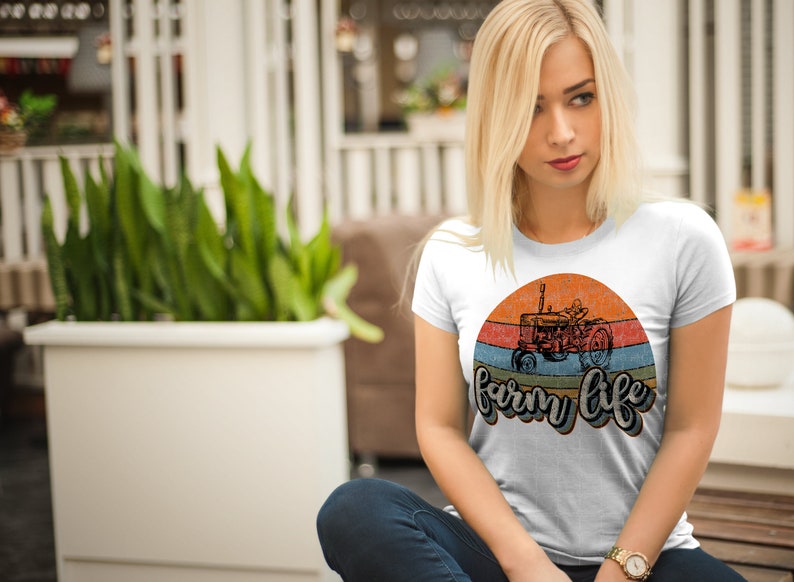 May include: White t-shirt with a vintage-style graphic of a tractor in front of a sunset with the text "farm life" in a retro font.