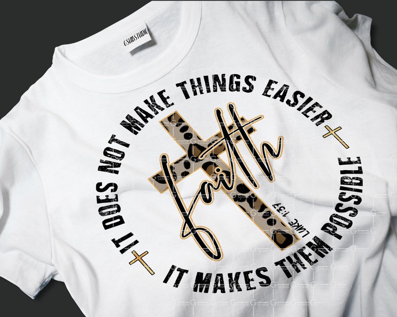 May include: White t-shirt with a black and gold graphic design. The graphic features a leopard print cross with the word "faith" written in a gold script. The text around the cross reads "It does not make things easier + It makes them possible" with the Bible verse "Luke 1:37" underneath.