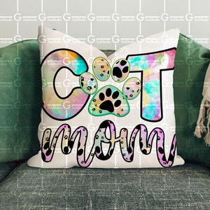 以下が含まれることがあります： 猫の足跡がついた「Cat Mom」と書かれたカラフルなタイダイ柄の白い枕。