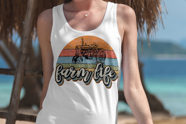 May include: White tank top with a vintage-style graphic of a red tractor in front of a sunset with the text "farm life" in a retro font.