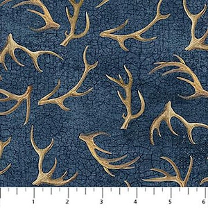 May include: A dark blue fabric with a black crackle texture pattern featuring a repeating print of tan deer antlers. A white ruler is visible at the bottom edge, showing measurements in inches from 1 to 6 inches across the bottom of the fabric.