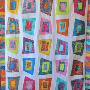 May include: A white quilt with a colorful geometric pattern. The quilt is made up of squares and rectangles of different colors and sizes. The squares and rectangles are arranged in a random pattern. The quilt is edged with a colorful border.