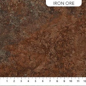 Puede incluir: Primer plano de una superficie marrón texturizada con apariencia moteada, que se asemeja al mineral de hierro. La superficie tiene una regla a lo largo del borde inferior, con medidas en pulgadas. El texto "IRON ORE" está en la esquina superior derecha.