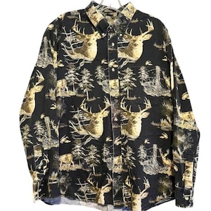 Puede incluir: Camisa negra con botones con un patrón repetido de cabezas de ciervos, árboles y otros elementos forestales en tonos beige y crema. La camisa de manga larga tiene cuello abotonado y puños abotonados.