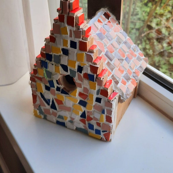 Nichoir mignon complètement dans le style d'une maison de canal d'Amsterdam. La maison est entièrement en mosaïque de différentes couleurs, le toit peut être détaché