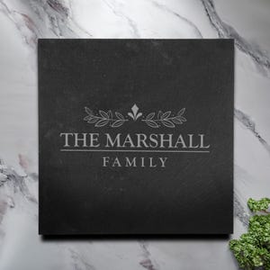 May include: Black slate sign with a white engraved design. The design features a stylised floral wreath with a crown at the top. The text "THE MARSHALL FAMILY" is engraved below the wreath.