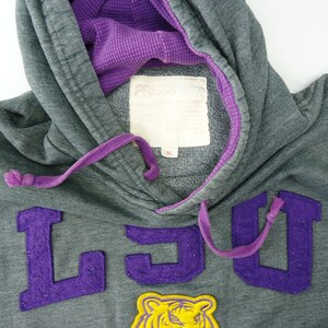 May include: Gray hooded sweatshirt with purple drawstrings and a purple and yellow LSU logo.