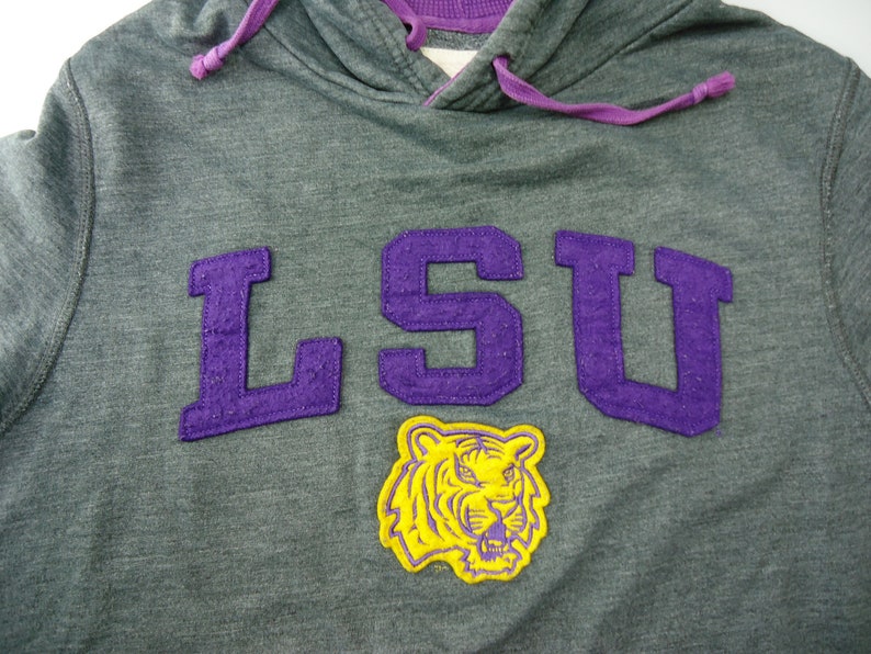 May include: Gray hooded sweatshirt with a purple LSU logo and a yellow tiger mascot.