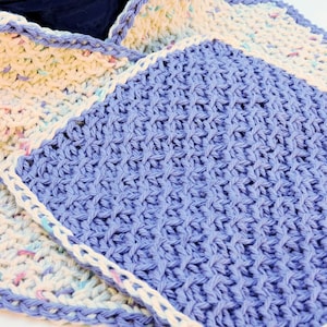 May include: Two knitted dishcloths, one is a light purple with a white border and the other is a cream color with a multi-colored border.