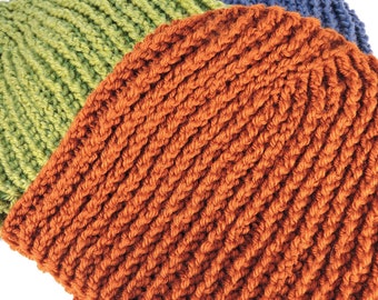 Könnte beinhalten: Eine gehäkelte Mütze in drei Farben: Orange, Grün und Blau. Die Mütze ist aus dickem Garn gefertigt und hat eine gerippte Struktur.