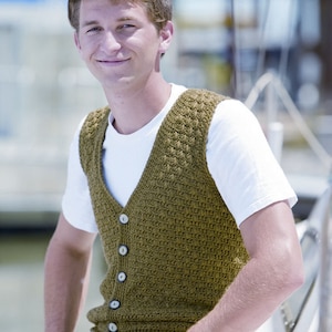 May include: A man wearing a brown knitted vest with buttons over a white t-shirt and blue jeans.