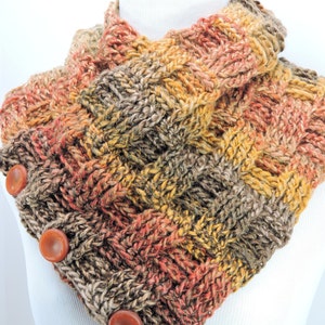May include: A knitted cowl neck scarf in shades of brown, orange, and yellow with a textured pattern. The scarf has three brown buttons on the side.