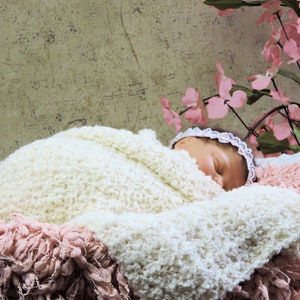 May include: A newborn baby sleeping peacefully in a white fuzzy blanket with pink fringe. The baby is wearing a white headband with a pink flower.