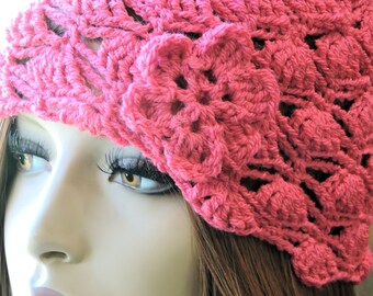 Può includere: Un cappello rosa all'uncinetto con un designo floreale. Il cappello è realizzato con un punto traforato delicato e ha un aspetto morbido e femminile.