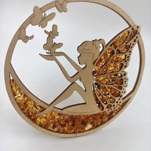 May include: A wooden fairy ornament with amber accents. The fairy is sitting on a crescent moon with wings made of amber pieces. There are four butterflies cut out of the wood.
