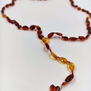 Puede incluir: Un collar de rosario de cuentas marrones y ámbar con un pequeño colgante de cruz de ámbar.