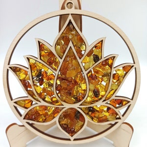 May include: A wooden circular wall hanging with a lotus flower design. The flower is filled with amber stones of various sizes and colors.